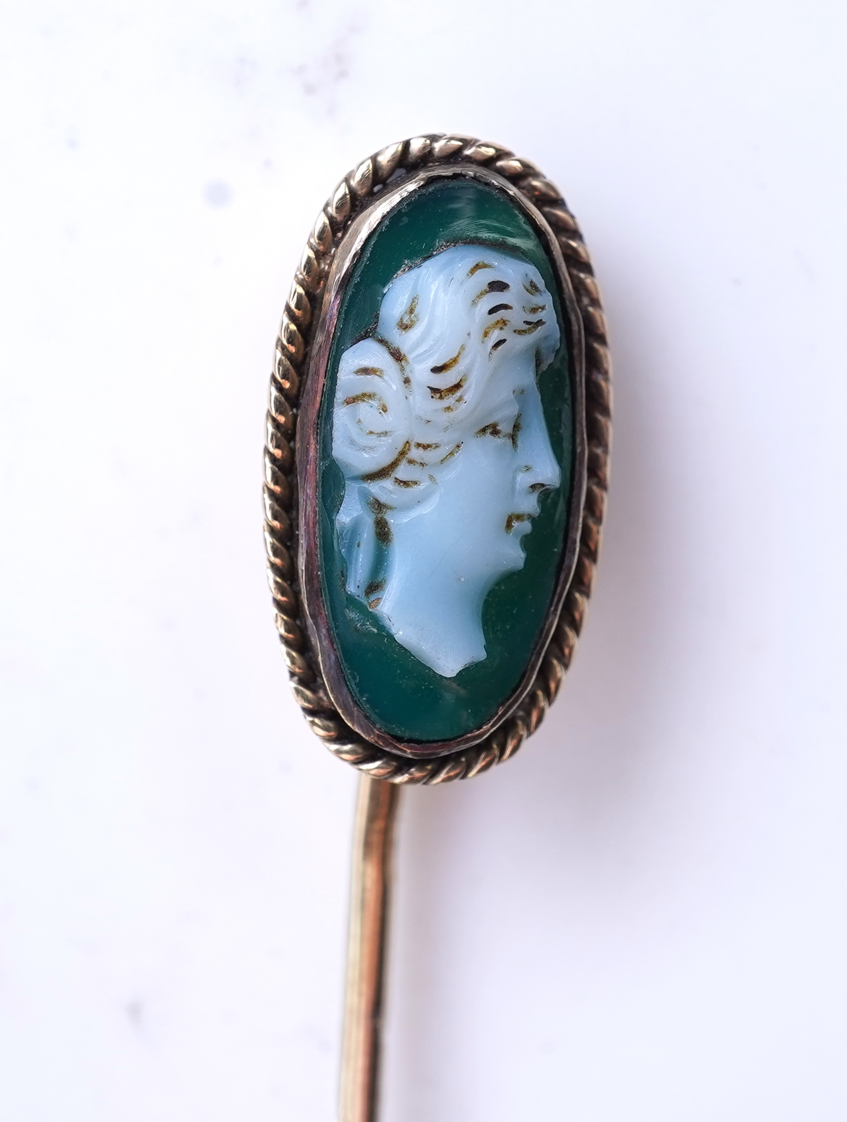 A collection of six stick pins, comprising: three gold stick pins, one set with a hardstone cameo, Austrian assay marks; a gold stick pin with a faceted edge; and a gold stick pin of Masonic design, stamped 9CT, combined